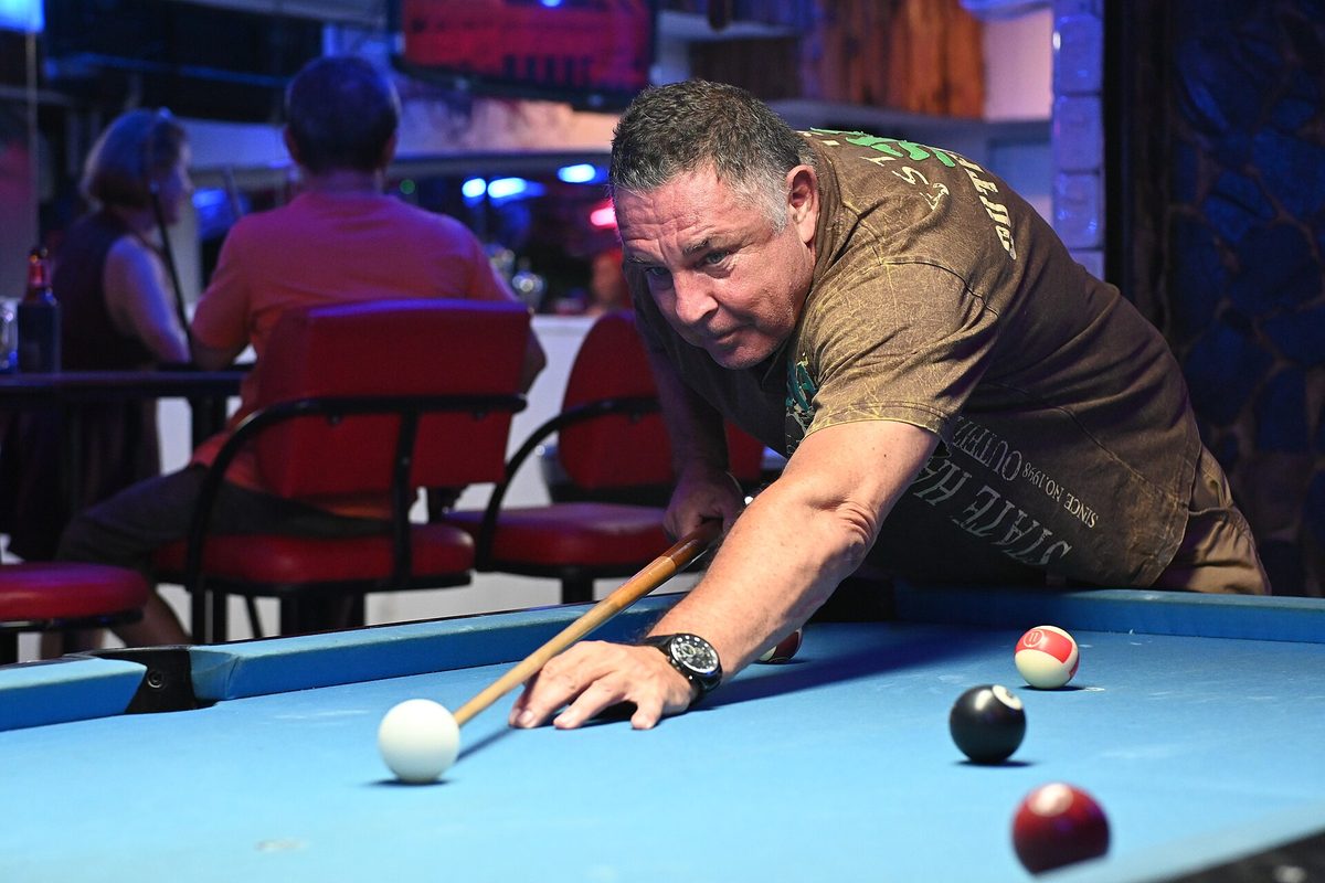 A player lines up in a dim billiards hall, eyes on the cue ball