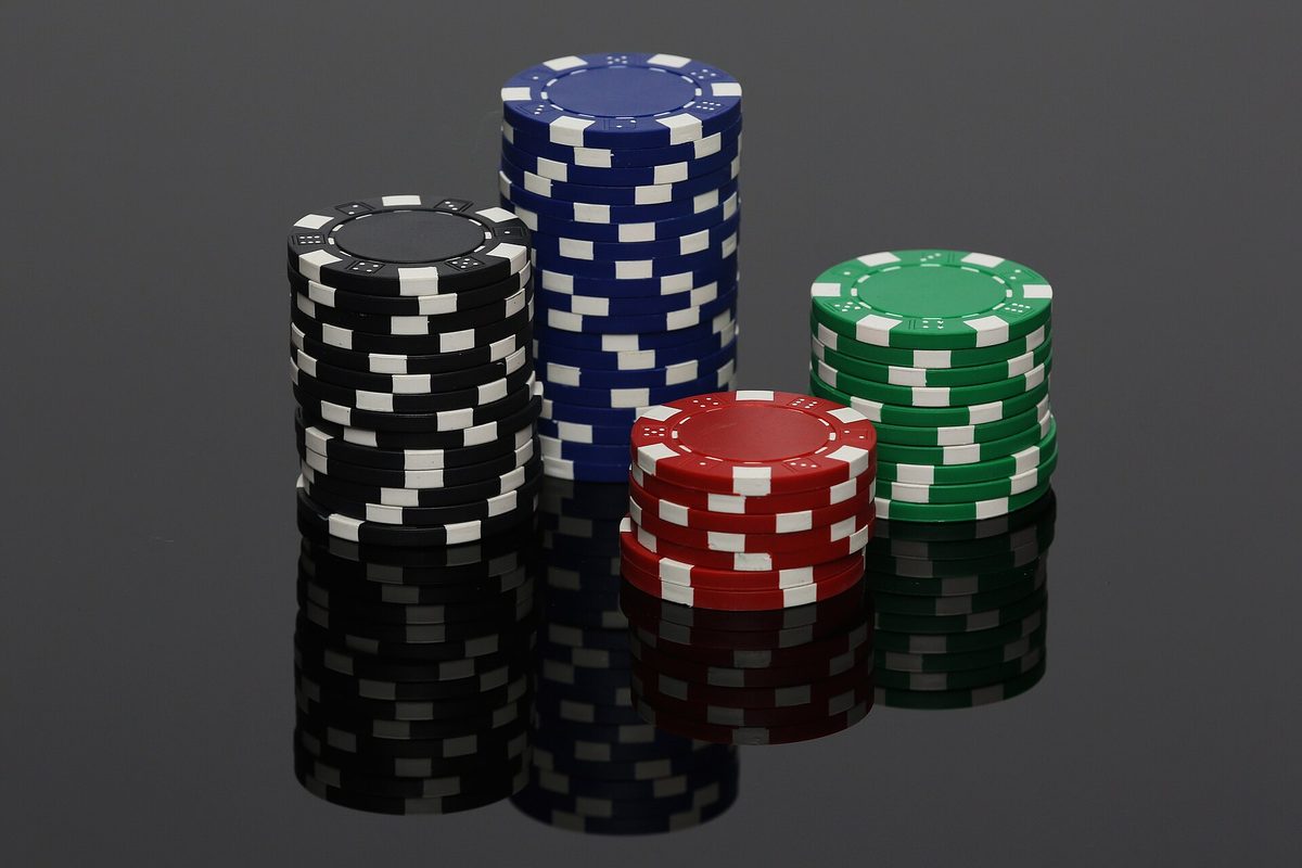 Four stacks of poker chips, black, blue, red and green, on a plain surface