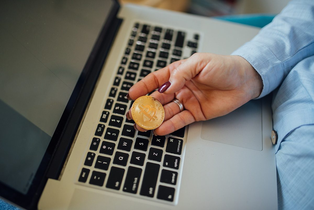 A physical bitcoin token held in one hand over a laptop keyboard