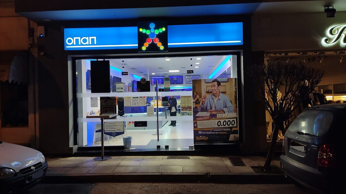 A betting shop lit up after dark on a street in Argos, Greece